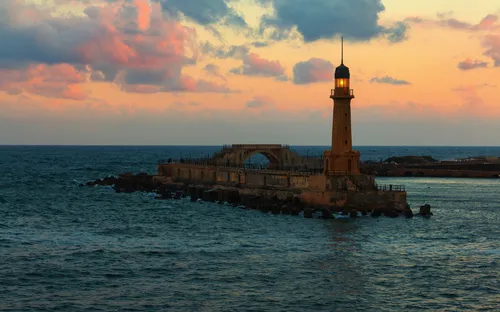 Leuchtturm auf einer Landzunge im Meer bei Sonnenuntergang.
