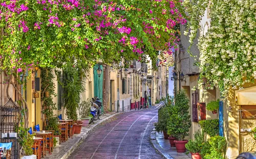 Malerische Straße mit Blumenranken und Café-Tischen in mediterranem Dorf.