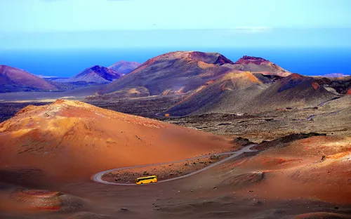 Gelbes Fahrzeug auf einer Straße durch eine vulkanische Berglandschaft.