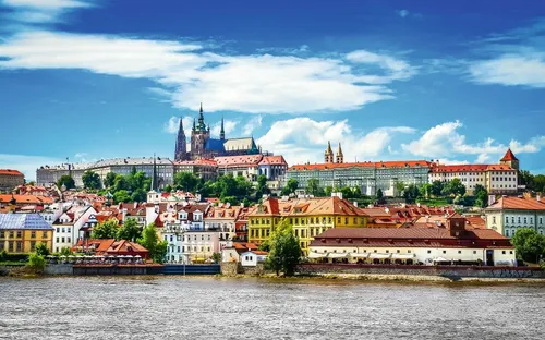 Panorama von Prag mit Fluss, historischen Gebäuden und Burg im Hintergrund.