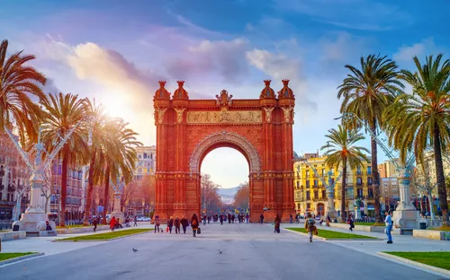 Triumphbogen in Barcelona bei Sonnenschein mit Menschen und Palmen umgeben.