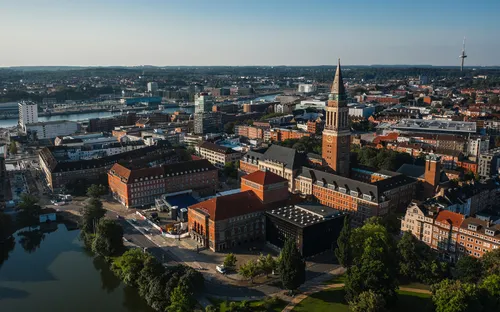 Luftaufnahme einer Stadt mit Fluss und Kirchturm im Zentrum.