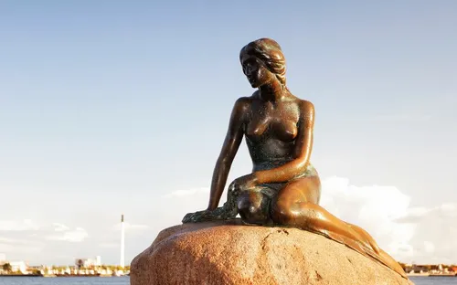 Statue einer sitzenden Meerjungfrau auf einem Felsen mit Blick auf das Wasser im Hintergrund.