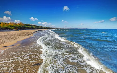 Ein sandiger Strand mit Wellen und blauem Himmel.