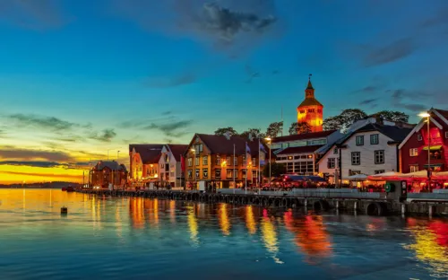 Hafenstadt bei Sonnenuntergang mit beleuchteten Gebäuden und ruhigem Wasser.