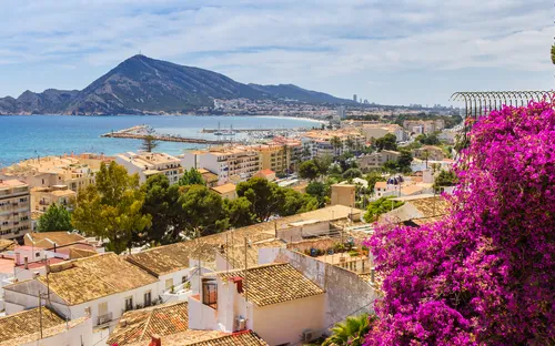 Stadtansicht mit Bougainvillea, Küste und Berg im Hintergrund bei sonnigem Wetter.