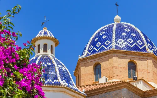 Kirche mit blauen Kuppeln und rosa Bougainvillea im Vordergrund.