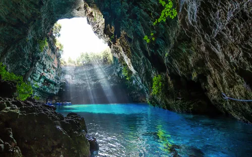 Lichtstrahlen in einer Höhle mit blauem Wasser und grünem Laub.