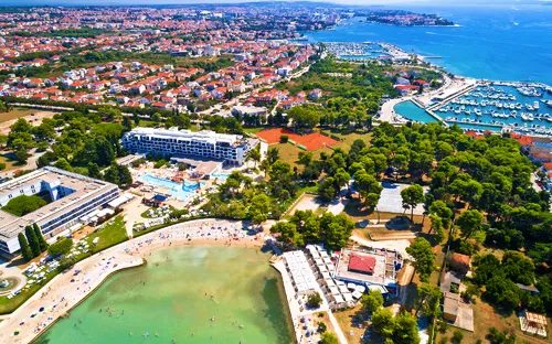 Luftaufnahme eines Küstenresorts mit Strand, Gebäuden und Hafen.