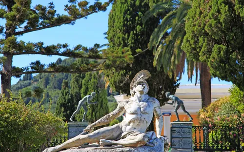 Eine antike Statue in einem Garten mit Bäumen und Pflanzen im Hintergrund.