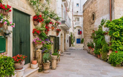 Eng verwinkelte Gasse mit üppigen Blumen und Pflanzen in einem mediterranen Dorf.