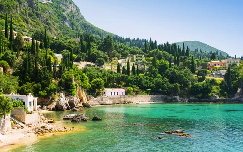Küste mit türkisfarbenem Wasser und Häusern in mediterraner Landschaft.