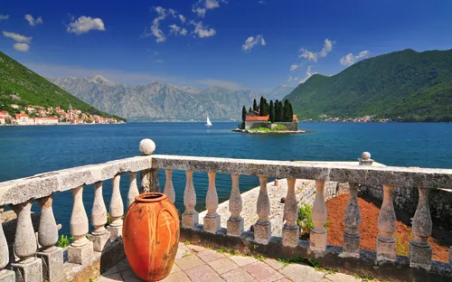 Blick auf eine Insel in der Bucht von Kotor mit See, Bergen und antikem Krug im Vordergrund.