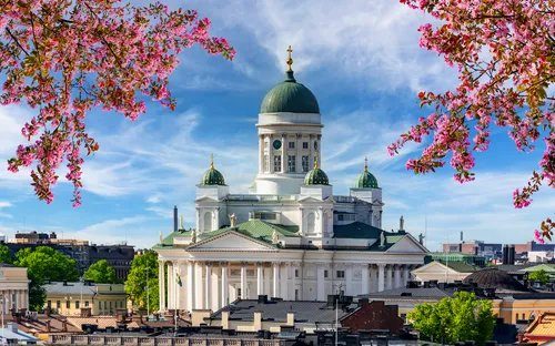 Kathedrale mit grünem Kuppeldach, umgeben von rosa Blüten und blauem Himmel.