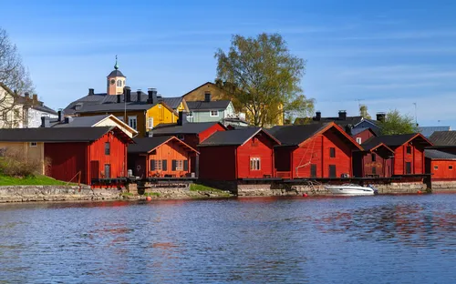 Rote Holzhäuser am Flussufer mit blauem Himmel.