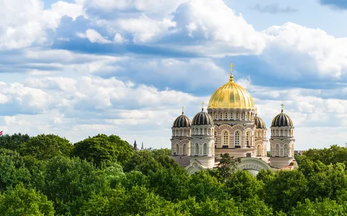 Kuppelkirche mit goldener Kuppel hinter Bäumen unter bewölktem Himmel.
