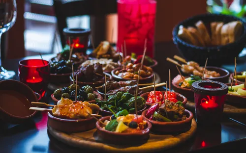 Verschiedene Tapas auf einem Tisch mit Kerzen und Brot im Hintergrund.