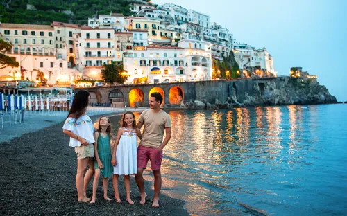 Familie am Strand vor beleuchteter Stadt an einer Küste in der Abenddämmerung.