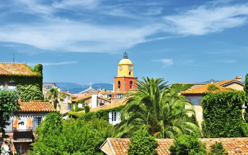 Stadtpanorama mit Kirchturm, Palmen und blauem Himmel.