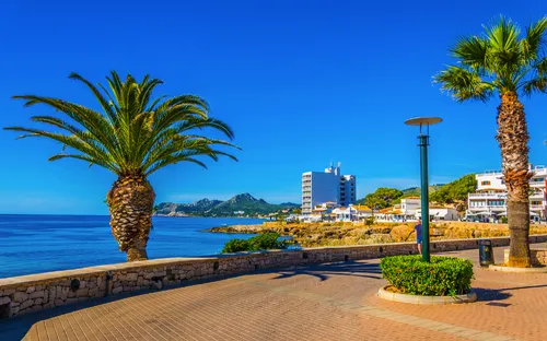 Promenade mit Palmen und Blick aufs Meer unter blauem Himmel.
