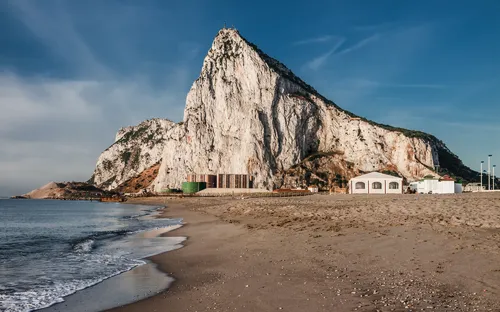 Küste mit Blick auf den Felsen von Gibraltar bei blauem Himmel und leicht bewölkt.