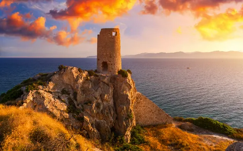 Steinruine auf einer Klippe mit Meer und Sonnenuntergang im Hintergrund