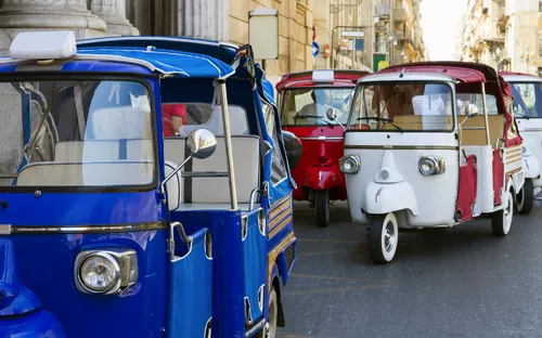 Drei bunte Tuk-Tuks fahren auf einer Stadtstraße.