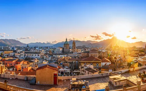 Panorama von Palermo bei Sonnenuntergang mit historischen Gebäuden und Bergen im Hintergrund.