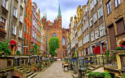 Historische Altstadtstraße mit Kopfsteinpflaster und bunten Gebäuden, Kirche im Hintergrund.
