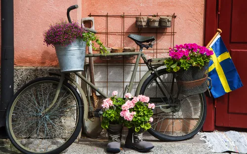 Fahrrad mit Blumenkörben, schwedische Flagge neben rotem Haus.