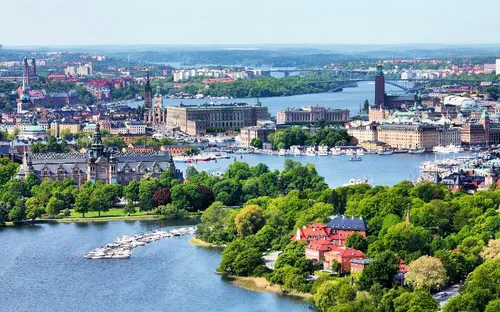 Stadtansicht mit Fluss, Brücken und grüner Landschaft im Vordergrund.