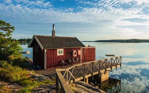 Rotes Holzhaus am Steg eines Sees bei sonnigem Wetter.