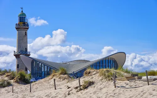 Leuchtturm und Gebäude in Dünen an der Ostsee unter blauem Himmel.