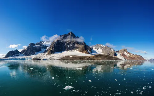 Berglandschaft mit Schnee, spiegelnd im eisbedeckten Wasser unter blauem Himmel.