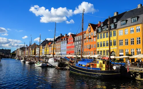 Bunte Häuserreihe am Wasser mit Segelbooten unter blauem Himmel.
