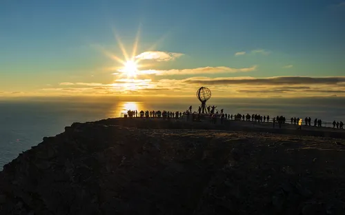 Sonnenuntergang am Nordkap mit Globus-Skulptur und Menschenmenge am Horizont.