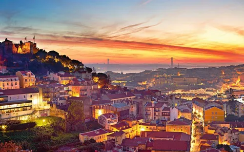 Blick auf Lissabon bei Sonnenuntergang mit Brücke und Burg auf einem Hügel.
