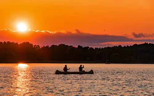 Zwei Personen paddeln in einem Kanu auf einem See bei Sonnenuntergang.