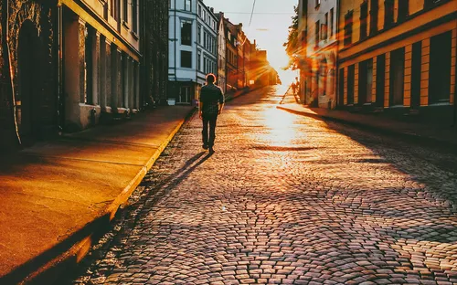 Person geht bei Sonnenuntergang auf gepflasterter Straße zwischen alten Gebäuden.