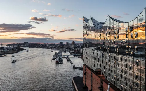 Blick auf die Elbphilharmonie in Hamburg bei Sonnenuntergang, Hafen und Elbe im Hintergrund.