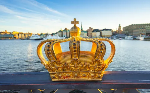 Goldene Krone auf einer Brücke mit Stadt im Hintergrund am Wasser.