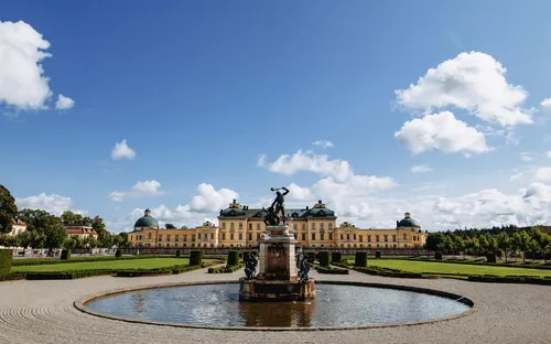 Barockes Schloss mit Springbrunnen und Gärten bei blauem Himmel.