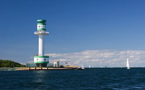 Leuchtturm am Meer mit Segelbooten im Hintergrund bei klarem Himmel
