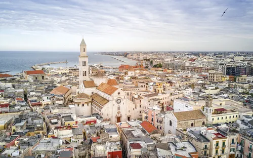Luftaufnahme einer Stadt mit historischer Kathedrale und Meer im Hintergrund.