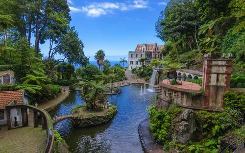 Garten mit Teich, Palmen, alten Gebäuden und Wasserfall an einem sonnigen Tag.
