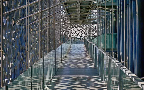 Metallische Brücke mit Gitterdesign und gläsernen Seiten, Schatten auf dem Boden.