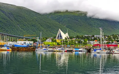 Hafen mit Segelbooten, Bergen im Hintergrund und eine moderne Kathedrale.