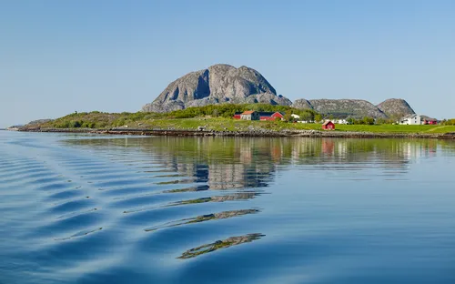 Fjordlandschaft mit Bergen und kleinen Häusern am Ufer unter klarem blauen Himmel