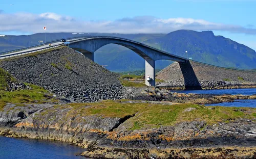 Brücke über felsige Küstenlandschaft mit Bergen im Hintergrund.