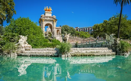 Springbrunnen und Statue in einem Park vor blauem Himmel und Palmen.